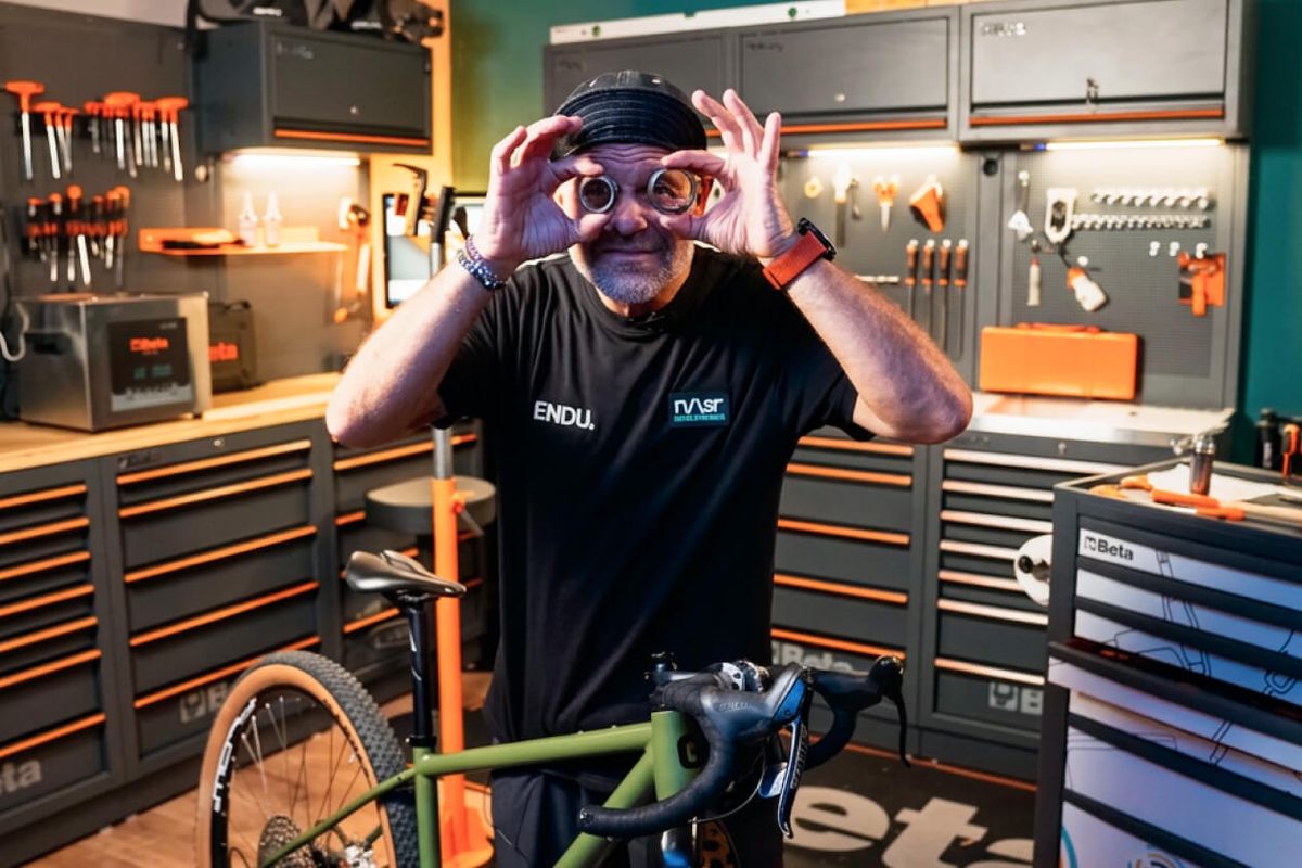 Gus Baldoni in officina tiene due cuscinetti della serie sterzo davanti agli occhi come fossero occhiali, con una bici gravel verde in primo piano