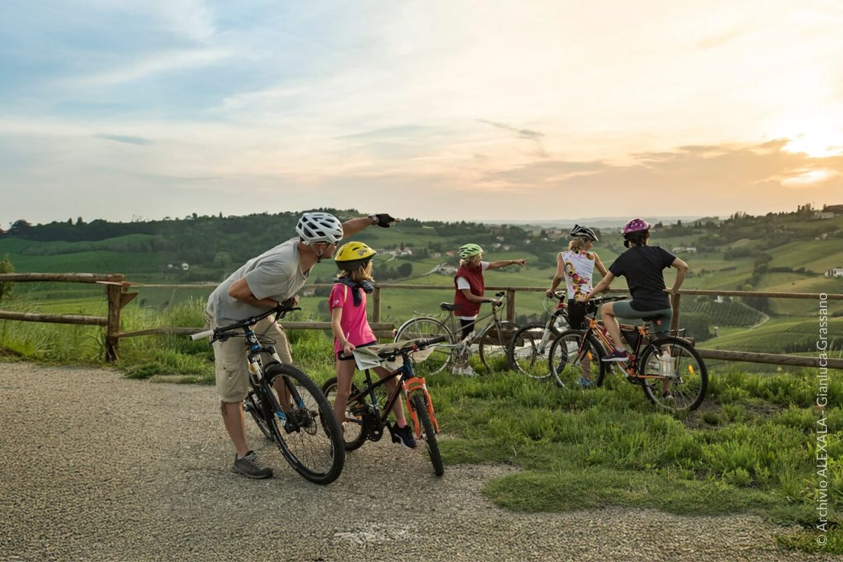 Una famiglia in bicicletta al tramonto su un belvedere panoramico tra le colline di Langhe, Roero e Monferrato